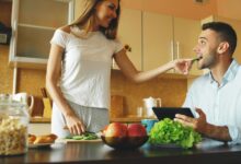 Un hombre durmiendo en una cama, con una mesa de despertador al lado, rodeado de frutas y verduras frescas