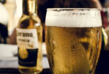Persona bebiendo cerveza en la playa, con un sol ardiente en el fondo