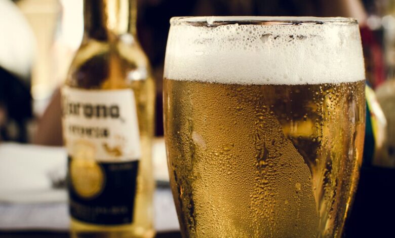 Persona bebiendo cerveza en la playa, con un sol ardiente en el fondo