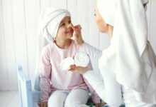 Niña aplicándose crema facial mientras revisa su piel en espejo