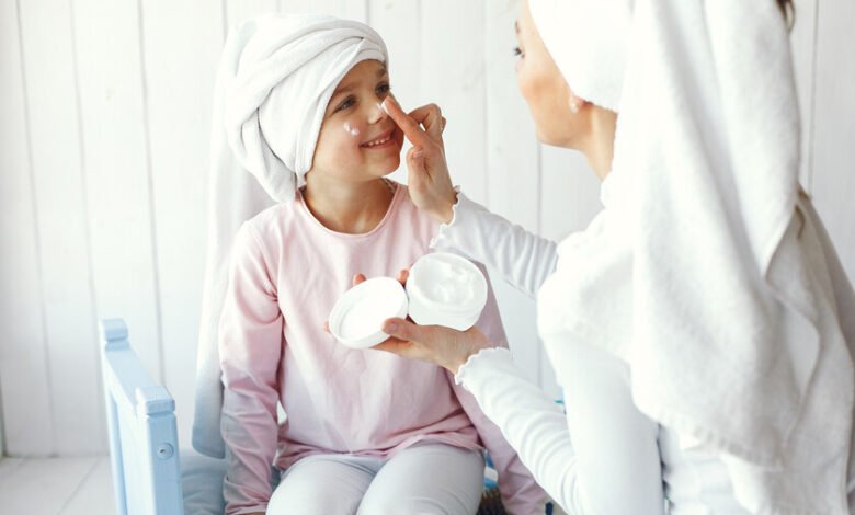 Niña aplicándose crema facial mientras revisa su piel en espejo
