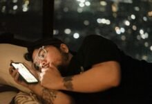 Persona con el móvil encendido en la cama, la pantalla ilumina la habitación